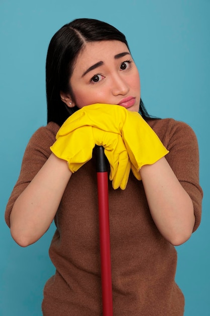 無料写真 落ち込んでいる疲れたアジアの主婦がブラシスティックを保持し、黄色の手袋をブラシスティックに保持し、家の掃除のコンセプト、家政婦が欲求不満を感じ、疲れ果てて休息をとる