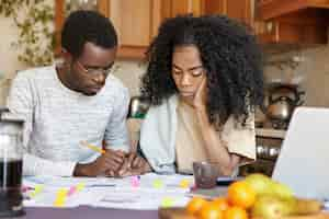 Free photo depressed unemployed african male in glasses having many debts holding his unhappy wife's hand