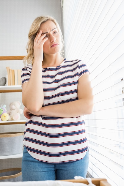 Depressed woman in deep thought standing near window