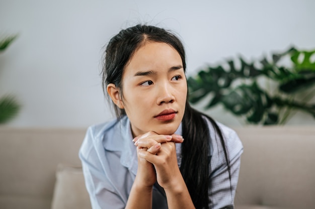 Depressed woman sitting on sofa at home, thinking about important things or feels unhappy with problem in personal life, copy space