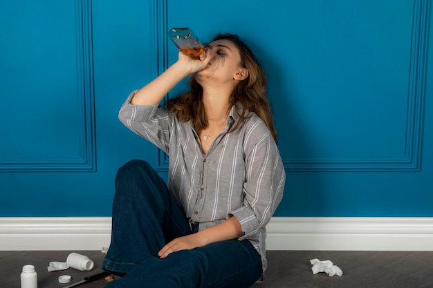 Depressed young girl sitting on the floor and drinking alcohol. High quality photo