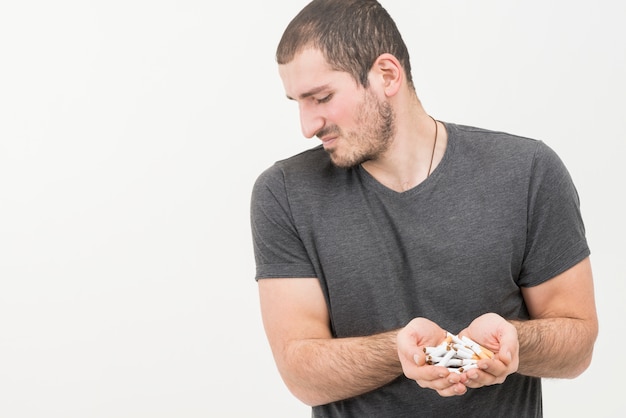 Бесплатное фото Подавленный молодой человек держит сломанные сигареты в руке на белом фоне