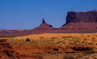 無料写真 乾燥した茂みと晴れた日に遠くに崖がある砂漠の丘