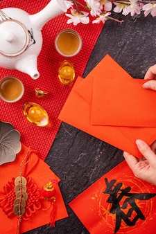 中国​の​月​の​1​月​の​新年​の​デザイン​コンセプト​-​幸運な​お金​の​ために​赤い​封筒​（​アンパウ​、​ホンバオ​）​を​持っている​女性​、​上面図​、​フラット​レイ​、​頭上​。 「​チュン​」​という​言葉​は​、​春​が​来る​こと​を​意味します​。