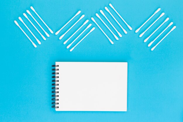 Design made with cotton swabs on blank spiral notepad on blue background