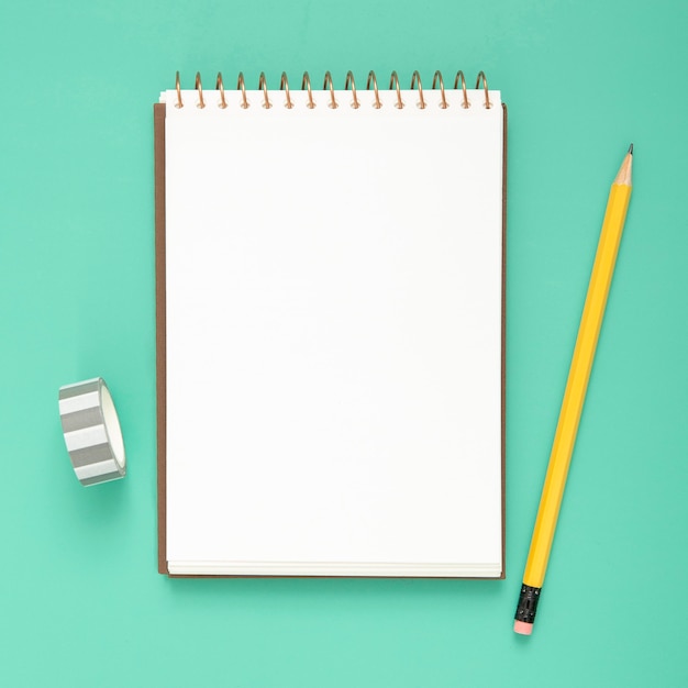 Desk arrangement with empty notepad on blue background