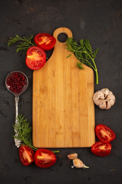 Le verdure dello scrittorio hanno affettato i pomodori e le verdure freschi maturi con aglio su un pavimento scuro