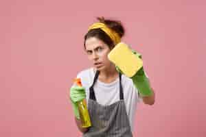 Бесплатное фото Отчаянная и скрупулезно аккуратная хозяйка моет окна губкой и спреем для мытья посуды во время уборки дома. молодая европейка в зеленых резиновых перчатках убирает на выходных