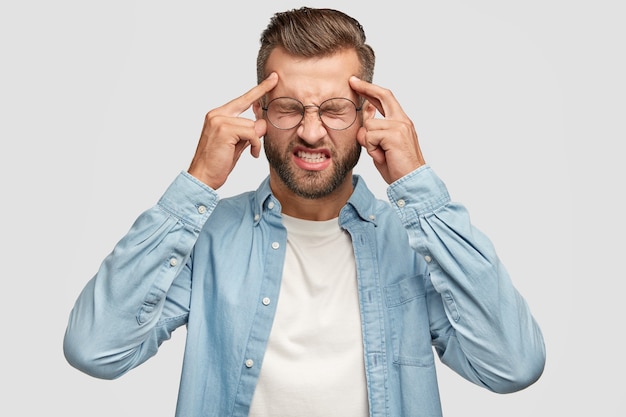 Desperate bearded guy posing against the white wall