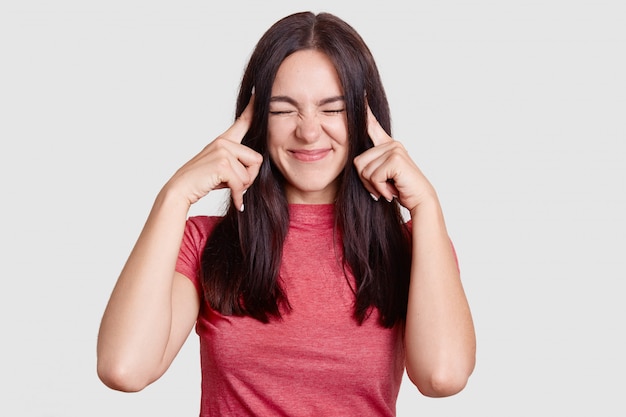 Desperate brunette woman keeps index fingers on temples, has terrible headache, tries to gather with thoughts