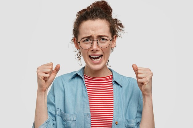 Desperate freckled teenager with glasses posing against the white wall