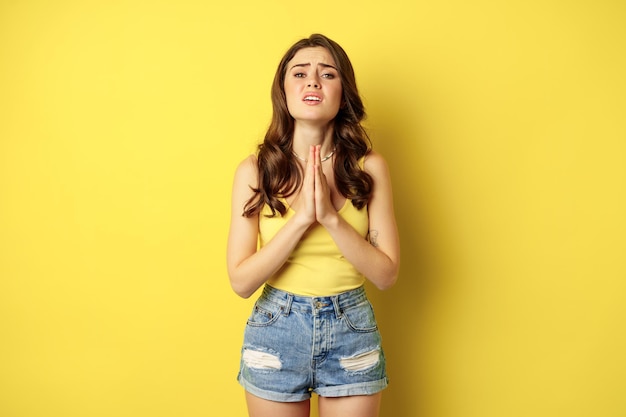 Desperate sad woman asking for help, begging with pray, need something, supplicating or praying, standing over yellow background