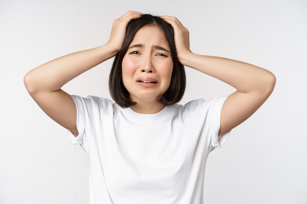 Desperate young korean woman holding hands on head panicking crying and standing distressed against white background