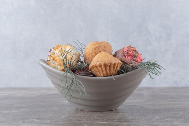 Dessert assortment on a small bowl adorned with pine leaves on marble surface