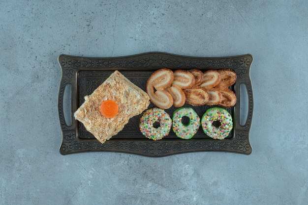 Dessert assortment with a cake slice, donut and flaky cookies on an ornate tray on marble surface