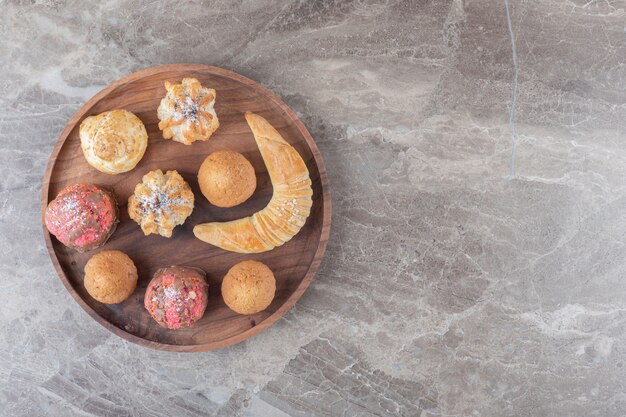 Dessert assortment with cookies, buns and cupcakes on a tray on marble surface