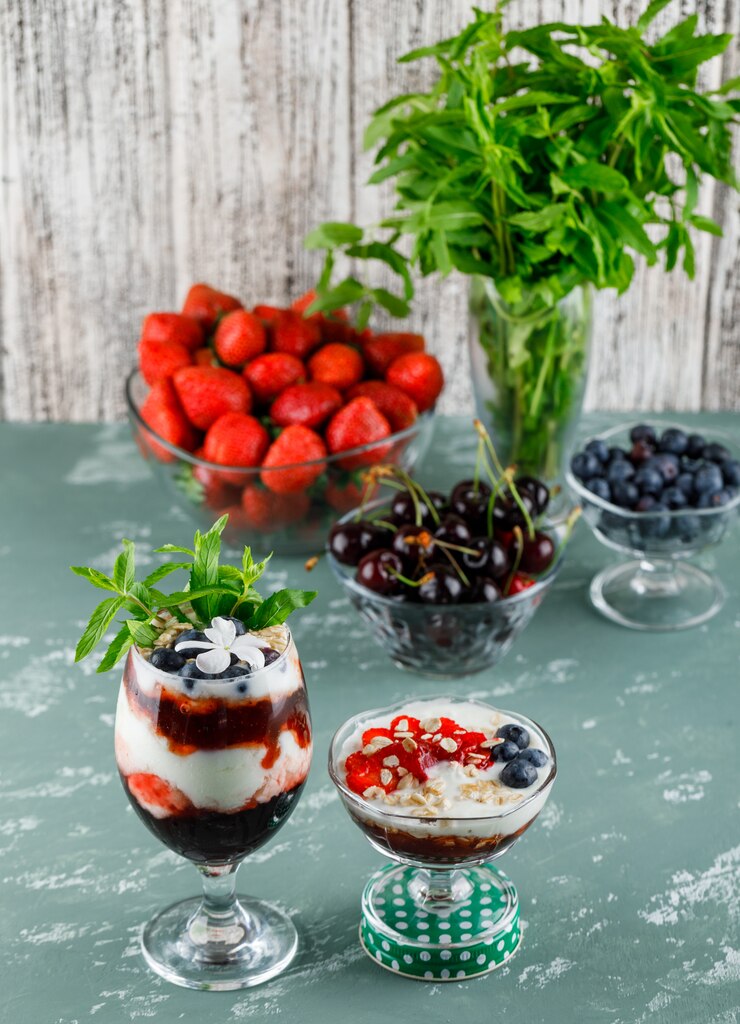 Free Photo dessert in vase and goblet with strawberries, blueberries, mint, cherries high angle view on plaster and grungy surface