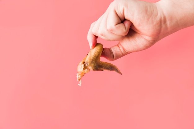 Free photo detail shot of person hand holding roasted chicken wings in front of pink background