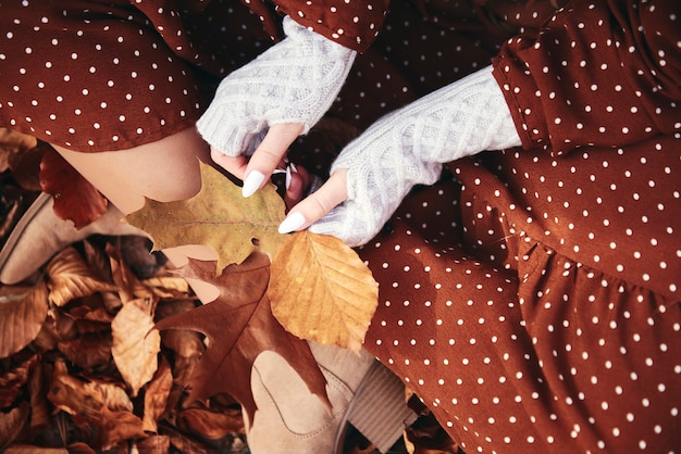 Foto gratuita particolare della donna seduta con un mazzo di foglie autunnali