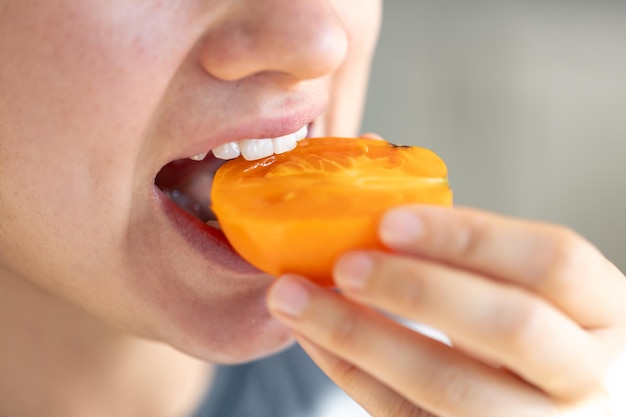 Free photo detailed shot of a woman bites yellow ripe tomato