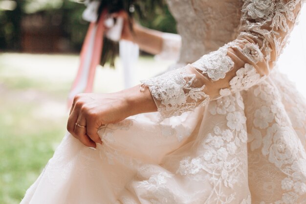 Details of bridal wedding dress, hand with wedding ring outdoors