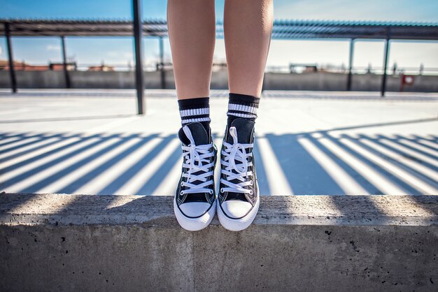 Details of woman legs standing on concrete ledge in her classic sneakers