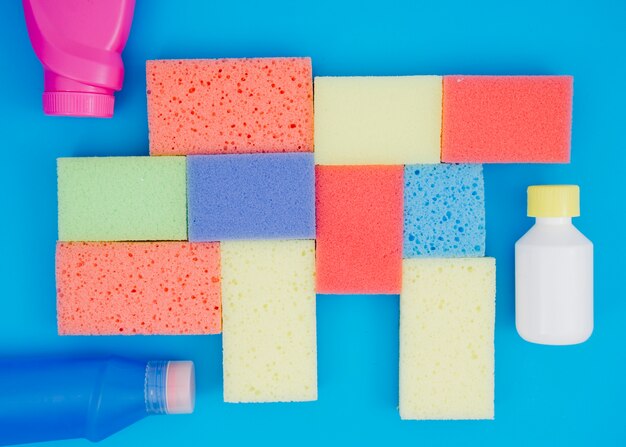 Detergent bottle near the multi colored sponges on blue background