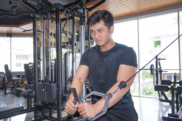 Determined Asian man exercising pecs on gym equipment