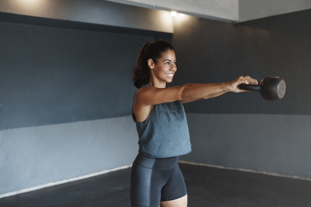 Kettlebell으로 혼자 체육관에서 운동하는 강한 히스패닉계 땀에 젖은 여자 결정