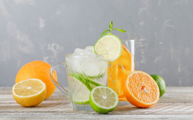 Вода вытрезвителя с известками, лимонами, апельсинами, мятой в чашке и стеклом на деревянном столе, взгляде со стороны.