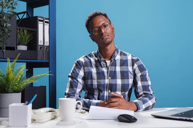 Development agency confident accountant sitting in workspace while looking at camera. Marketing company serious firm office worker sitting at desk in agency modern interior.