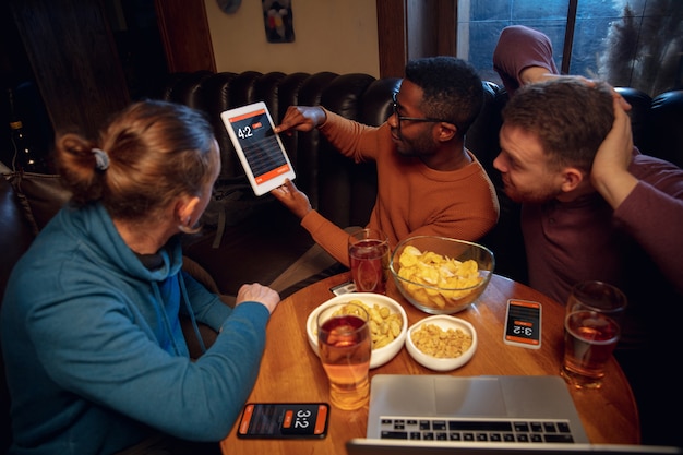 Device screen with mobile app for betting and score. Device with match results on screen, excited fans on background during match.