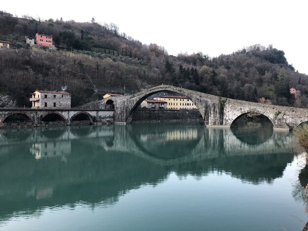 Devil Bridge surrounded by hills covered in forests reflecting on the lake in Borgo a Mozzano