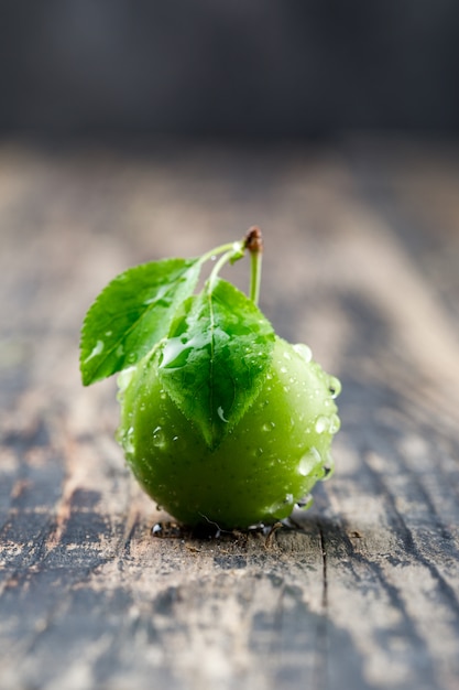 Dewy green plum with leaves side view on wooden and grungy wall