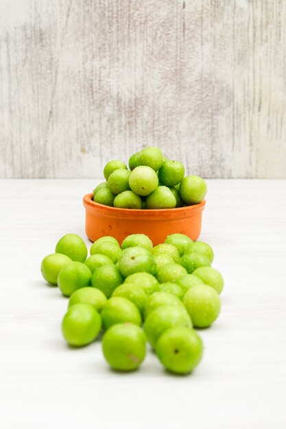 Dewy green plums in a round clay bowl side view on white and grunge