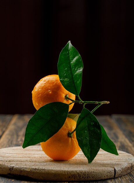 Dewy oranges on a wooden board with branch side view on black and wooden table