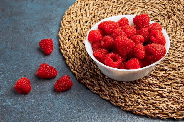 Dewy raspberries in a white bowl high angle view on a abstract grunge and wicker placemat background