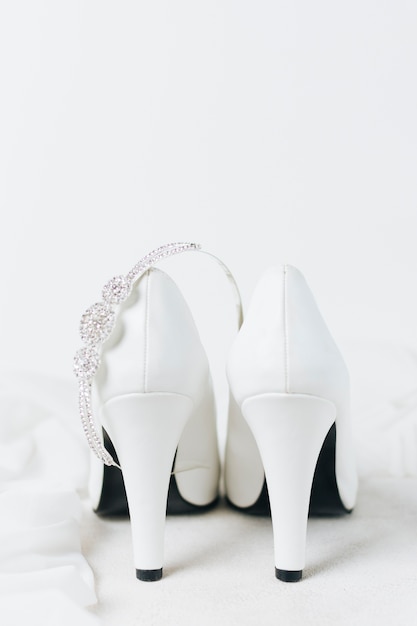 Free photo diamond crown over the pair of white wedding high heels against white backdrop