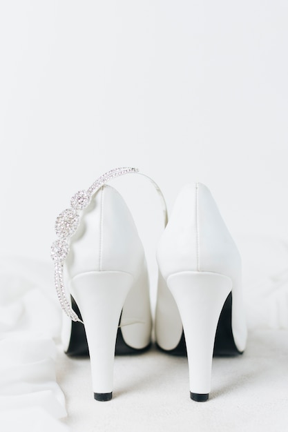 Diamond crown over the pair of white wedding high heels against white backdrop