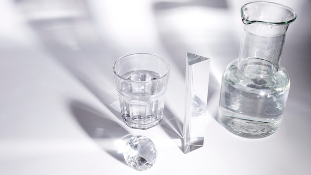 Free photo diamond; glass of water; prism and beaker with shadow on white backdrop