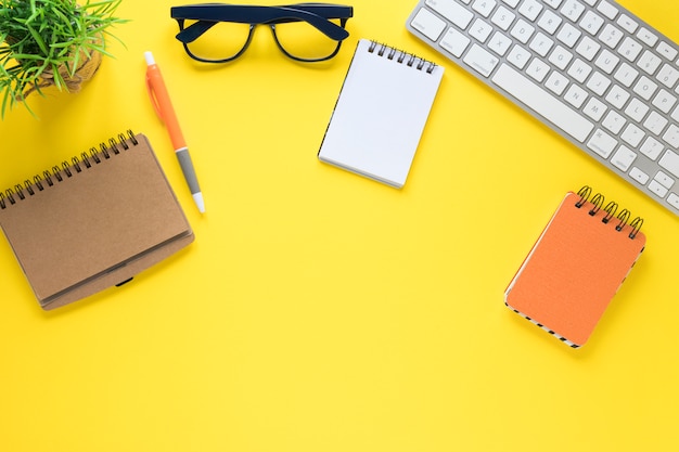 Diary; pen; spiral notepad; eyeglasses and keyboard on yellow background