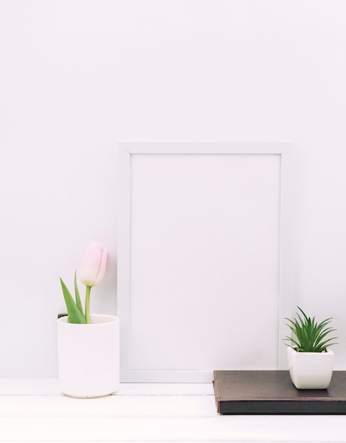 Diary; plant; tulip flower with blank photo frame on white table