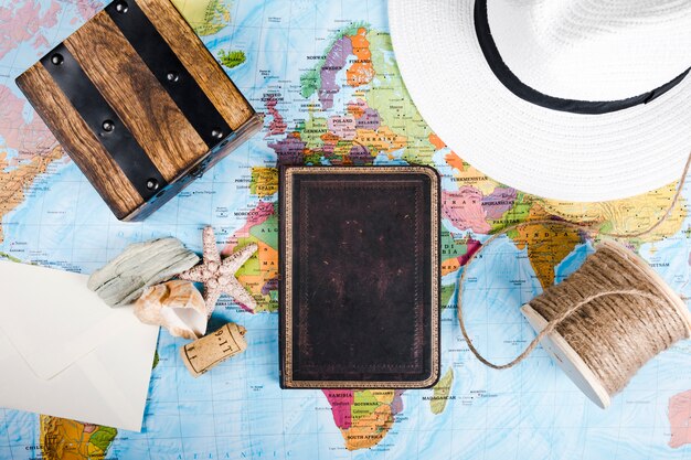 Diary, sea shell, hat, wooden box, and spool, on world map