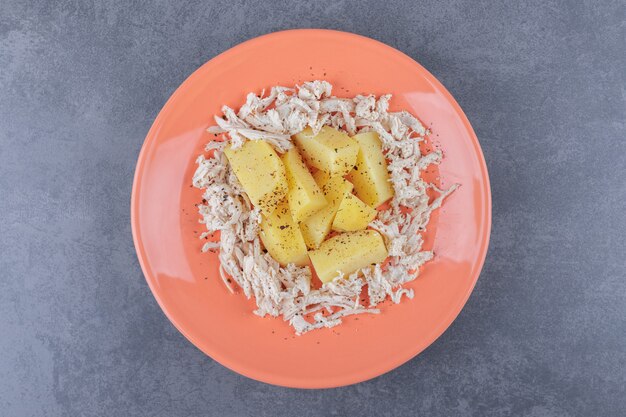 Diced chicken with boiled potatoes on orange plate.