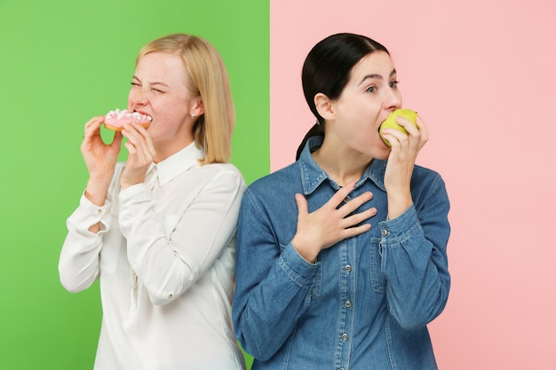 ダイエット。ダイエットのコンセプトです。健康食品。果物と不気味なケーキの間を選択する美しい若い女性