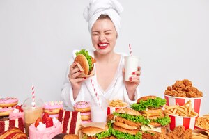 無料写真 ダイエットの失敗と不健康なライフスタイルの概念。大喜びの若い女性はハンバーガーと炭酸飲料を保持します