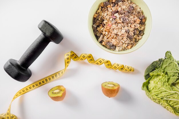 Diet food with dumbbell and measuring tape on white background