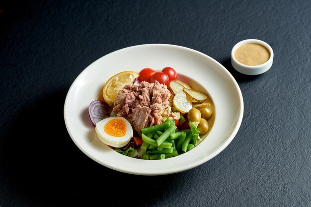 Диетический салат нисуаз с тунцом, яйцом и спаржей в белой тарелке на черном фоне