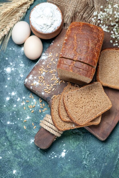 Above of dietary black bread wheats on wooden board spikes flower eggs flour in bowl on blue background