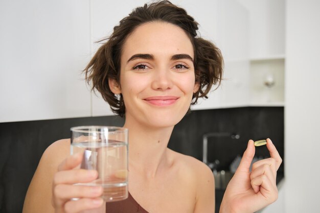 栄養補助食品と健康的なライフ スタイル st のコップ一杯の水でビタミン CD オメガを摂取する若い女性